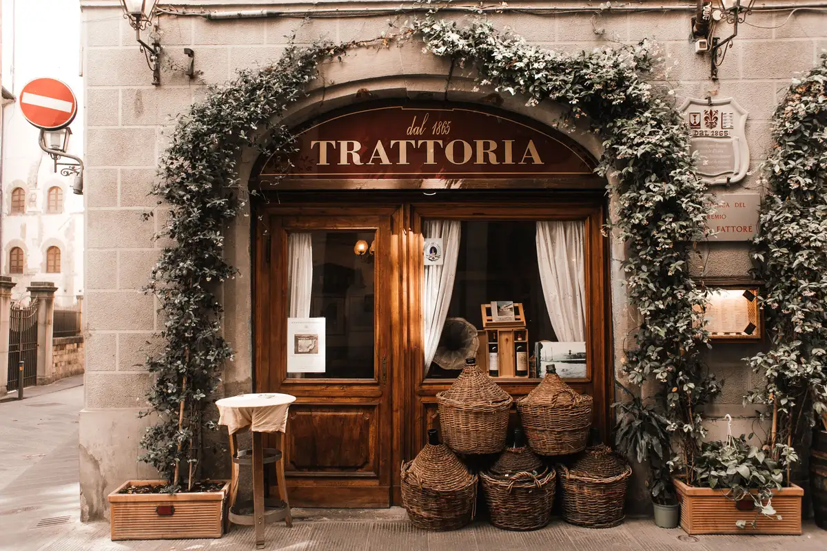 Ivy-covered trattoria storefront with wooden doors, hanging wine baskets, and a vintage sign