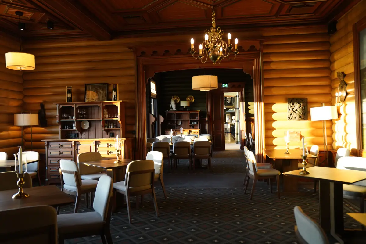Empty rustic restaurant dining room with log walls, chandelier, and warmly lit tables set for guests