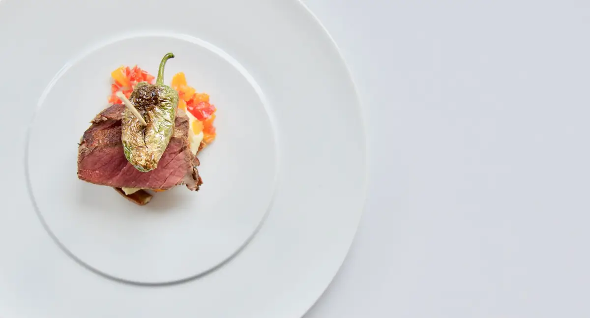 Overhead view of a single fine-dining plated course with sliced meat, roasted pepper, and citrus garnish