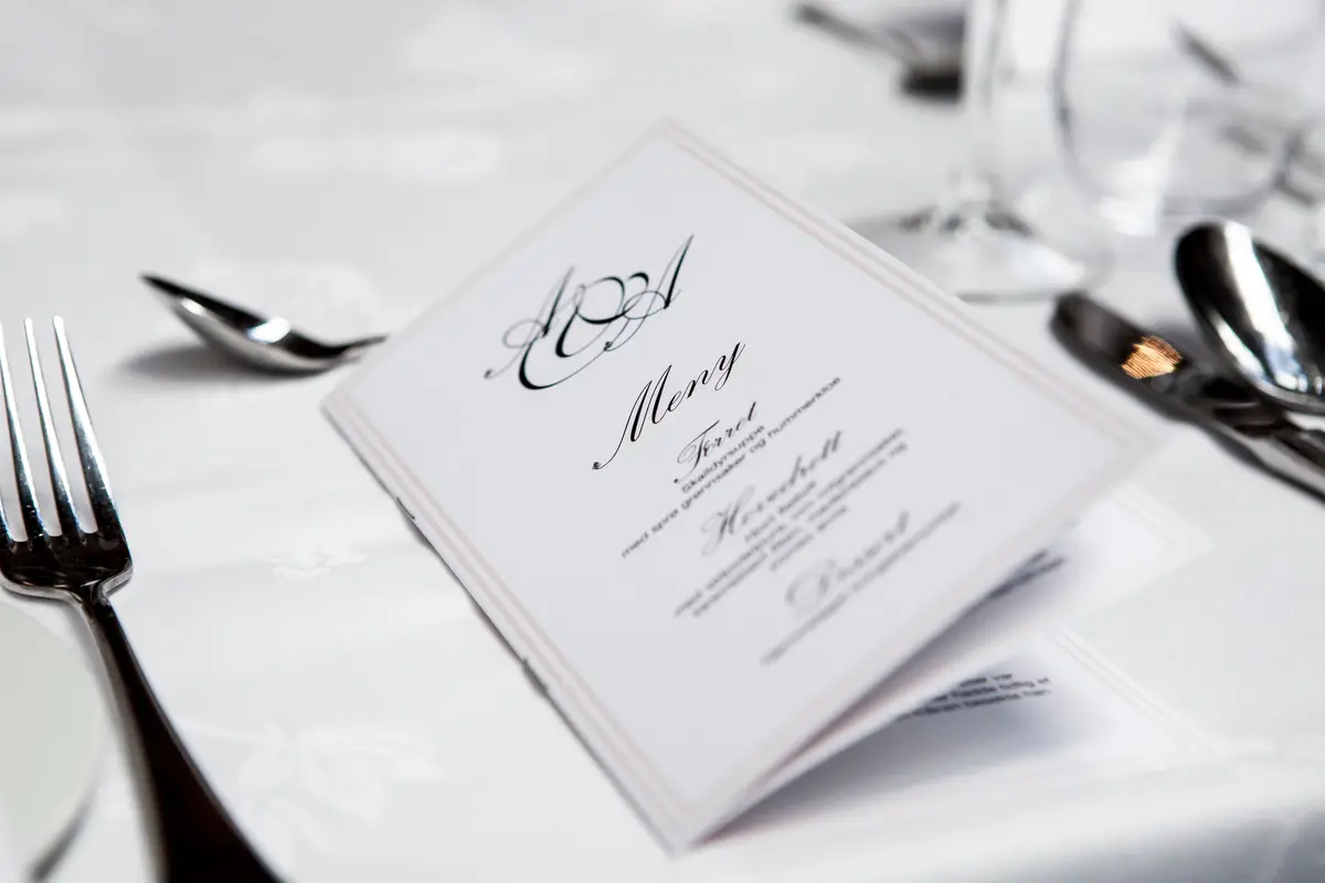 Folded printed menu card standing on a white-clothed table beside silverware and a wine glass
