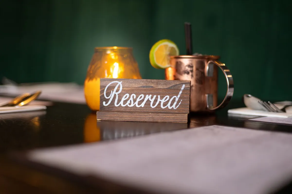 A wooden Reserved sign on a dark restaurant table beside a candle and a copper mug, before service