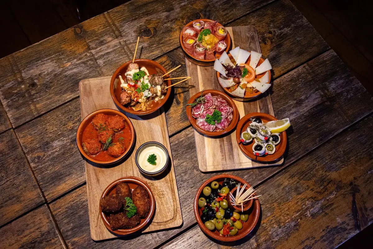 Assorted tapas-style small plates on wooden boards spread across a rustic shared table