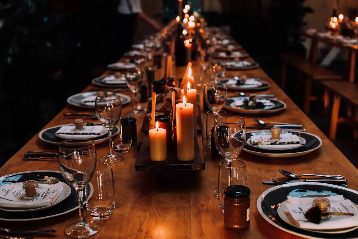 Long candlelit wooden communal table set with white plates, wine glasses, and place cards