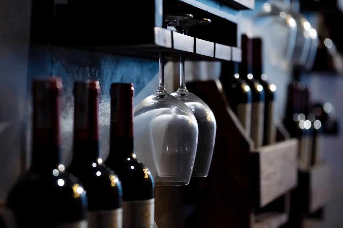 Red wine bottles and hanging wine glasses on a dark wood bar rack